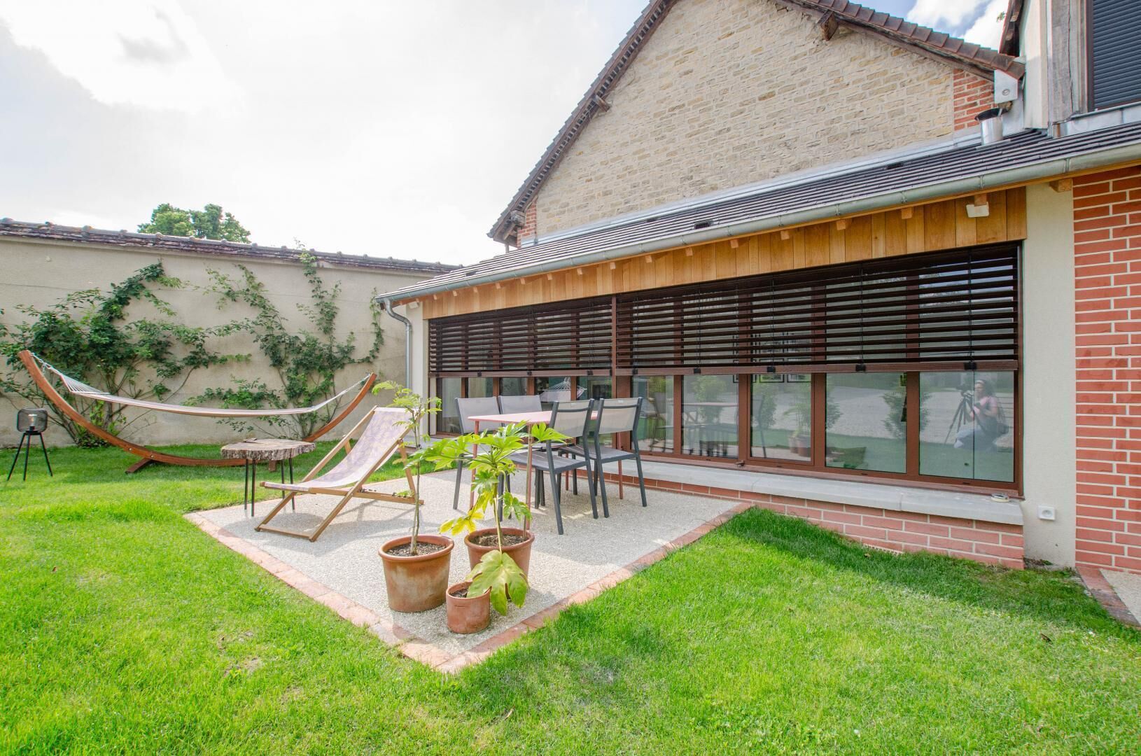 Un jardin avec un hamac, des chaises, une table et des plantes en pot.