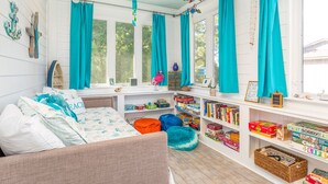 Una habitación acogedora con una cama, un rincón de lectura junto a la ventana con libros y vistas a árboles.