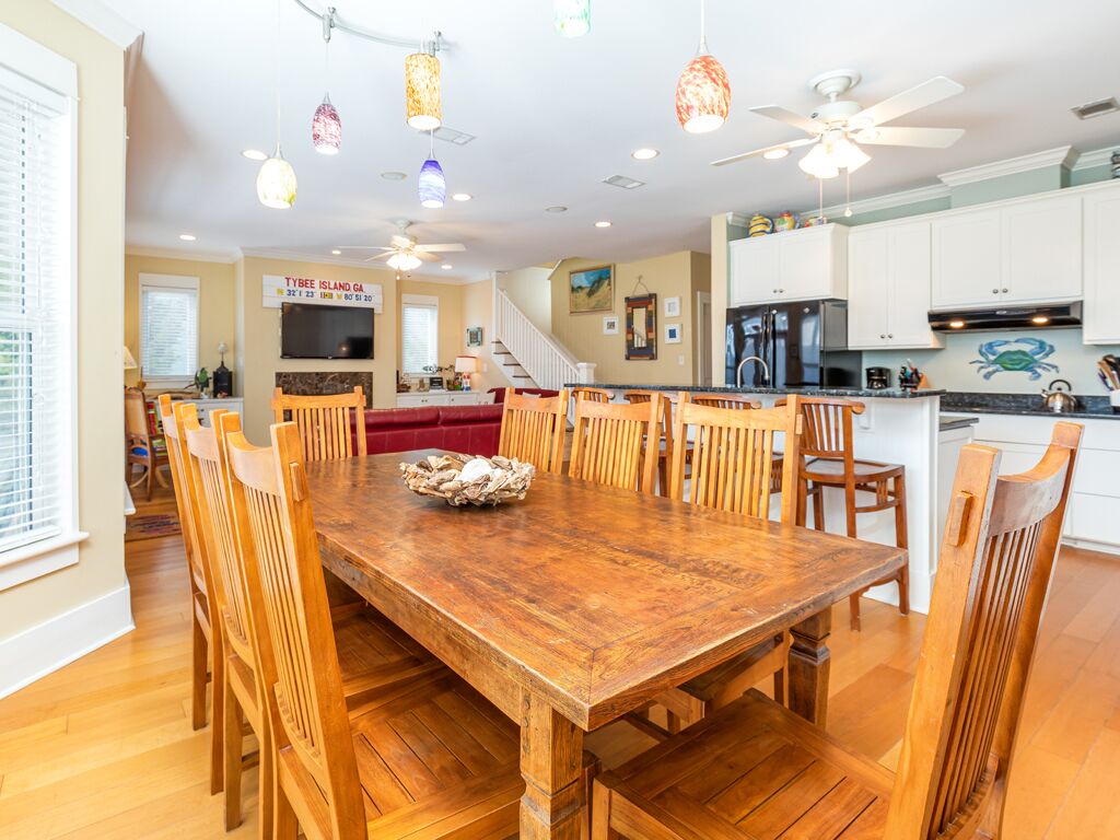 A spacious dining area with a wooden table and chairs, a kitchen with white cabinets, and a ceiling fan.