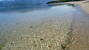 A beach with clear shallow waters revealing pebbles and shells, a sandy shore, and distant mountains. - Mountain house with panoramic viewpoint.  (Florianópolis)