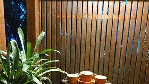 A wooden partition with vertical slats, a small wooden table with three orange containers, and a potted plant with long green leaves. - Mountain house with panoramic viewpoint.  (Florianópolis)