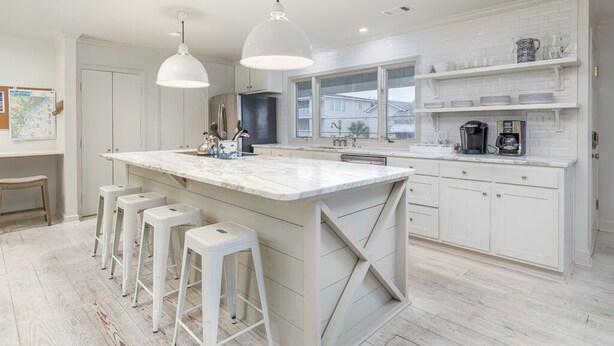 A modern kitchen with a large island, bar stools, white cabinetry, and pendant lighting. - High Tide by Tybee Vacation Rentals (Tybee Island)
