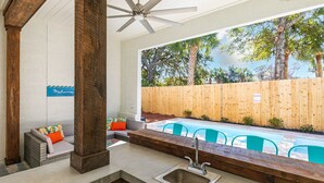 A poolside area with a built-in sink, a ceiling fan, and a view of a wooden fence and trees. - High Tide by Tybee Vacation Rentals (Tybee Island)