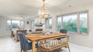 A spacious dining area with a wooden table, blue-striped chairs, and a hanging light fixture. - High Tide by Tybee Vacation Rentals (Tybee Island)