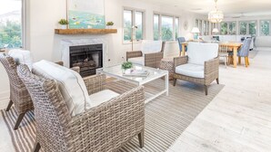 A spacious living room with wicker furniture, a fireplace, and large windows offering a view of the outdoors. - High Tide by Tybee Vacation Rentals (Tybee Island)