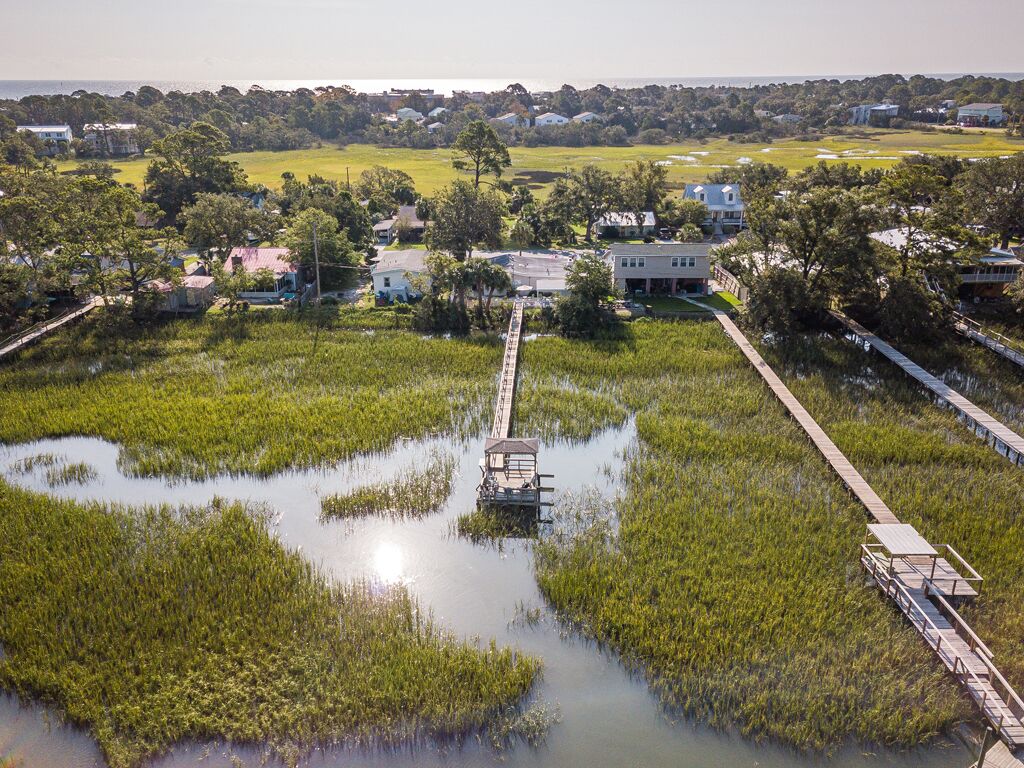 Zona costera con un puente de madera que lleva a una casa rodeada de agua y vegetación.