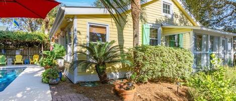 A yellow house with a pool, surrounded by greenery and a palm tree.