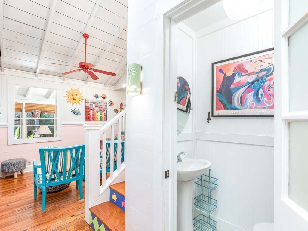A bright, well-lit room with a wooden floor, a red ceiling fan, a white door, and a large window.