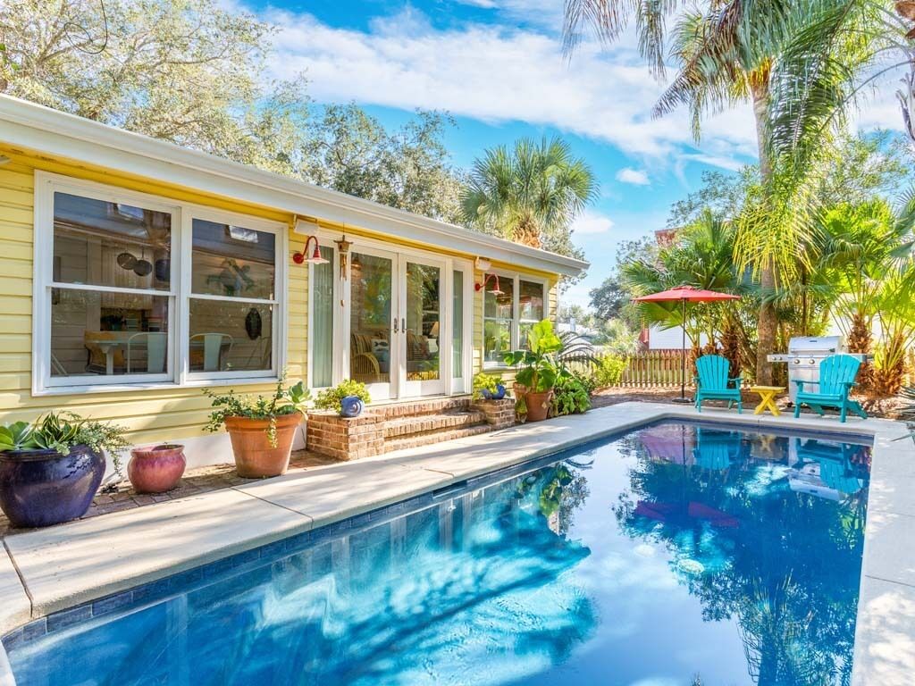 A poolside area with a house, potted plants, and outdoor furniture.