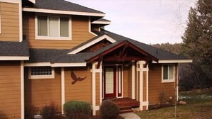 Une maison à deux étages avec un porche à l’avant, une porte rouge et une sculpture d’oiseau sur le mur.