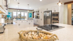 A modern kitchen with white cabinets, stainless steel appliances, and a large island with a woven basket of seashells.