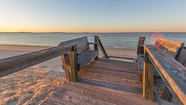 A wooden boardwalk leading to a beach with a clear sky.