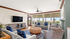 A spacious living room with a large TV, comfortable seating, and a view to the outdoors.