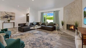 A modern living room with a sectional sofa, a round coffee table, and a fireplace. - Pool, Hot Tub, Al Fresco Dining, Gazebo | Pet-Friendly Desert Haven | Catalina (Palm Springs)