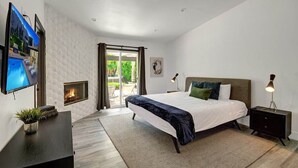 A modern bedroom with a large bed, a TV, a fireplace, and a view of the outdoors. - Pool, Hot Tub, Al Fresco Dining, Gazebo | Pet-Friendly Desert Haven | Catalina (Palm Springs)