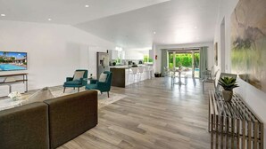 A spacious living area with a sofa, teal armchairs, a coffee table, and a TV. A kitchen with a bar is visible in the background. - Pool, Hot Tub, Al Fresco Dining, Gazebo | Pet-Friendly Desert Haven | Catalina (Palm Springs)