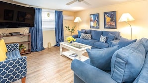 Un salon avec un canapé bleu, une table basse, un téléviseur et un ventilateur de plafond.