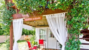 Un espace extérieur aménagé avec une zone de sièges couverte, un tapis à motifs floraux, deux chaises rouges et une enseigne indiquant « KANUNA KABANA ».