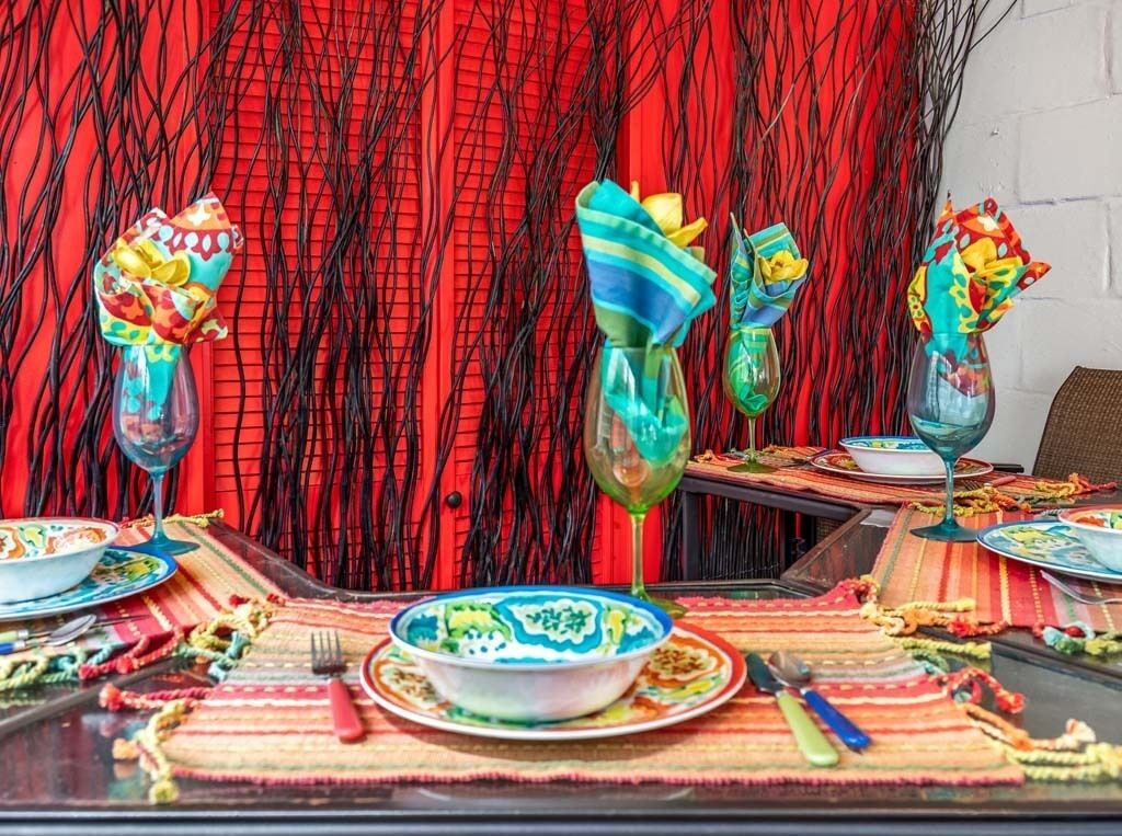 Een eettafel gedekt met kleurrijke tafelkleden, servies en glazen.