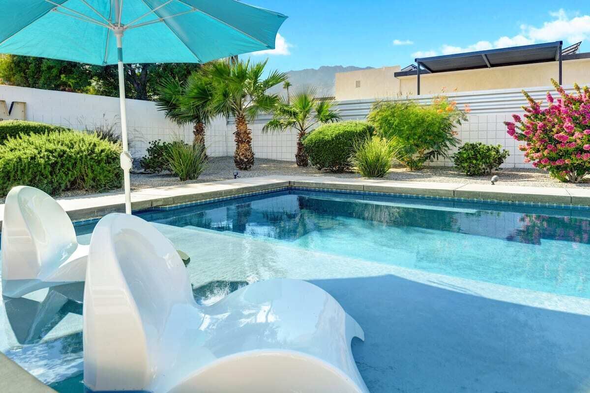 Una piscina amb aigua cristal·lina blava, envoltada de gandules blanques i un parasol blau.