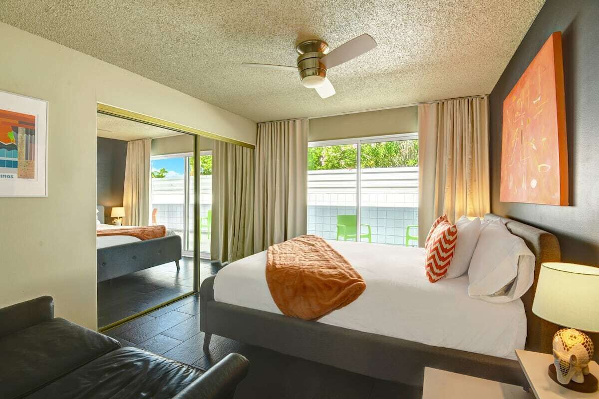 Habitación de hotel con cama, escritorio, silla, ventilador de techo y vistas al exterior.