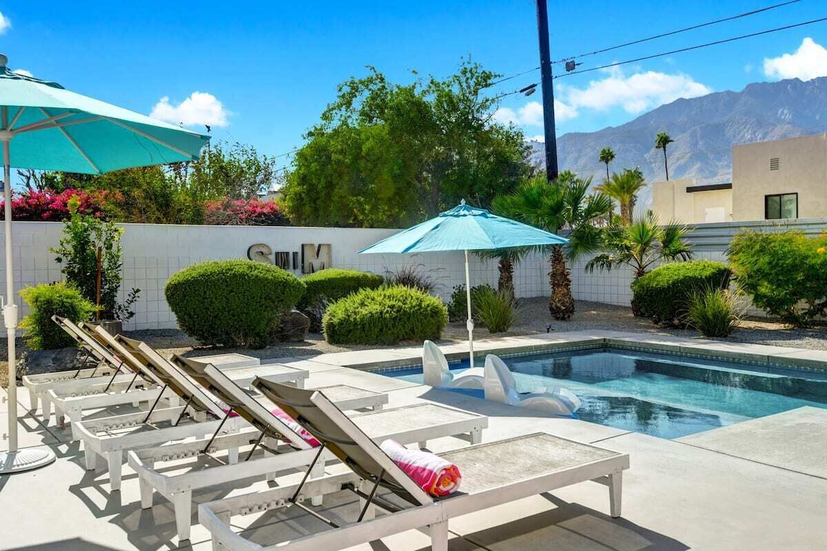 Un espace piscine agrémenté de chaises longues et de parasols, entouré d’un aménagement paysager soigné et avec une chaîne de montagnes en toile de fond.