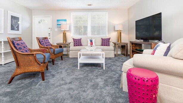 Ein Wohnzimmer mit einer Couch, zwei Sesseln, einem Couchtisch, einem Fernseher und einer Lampe.