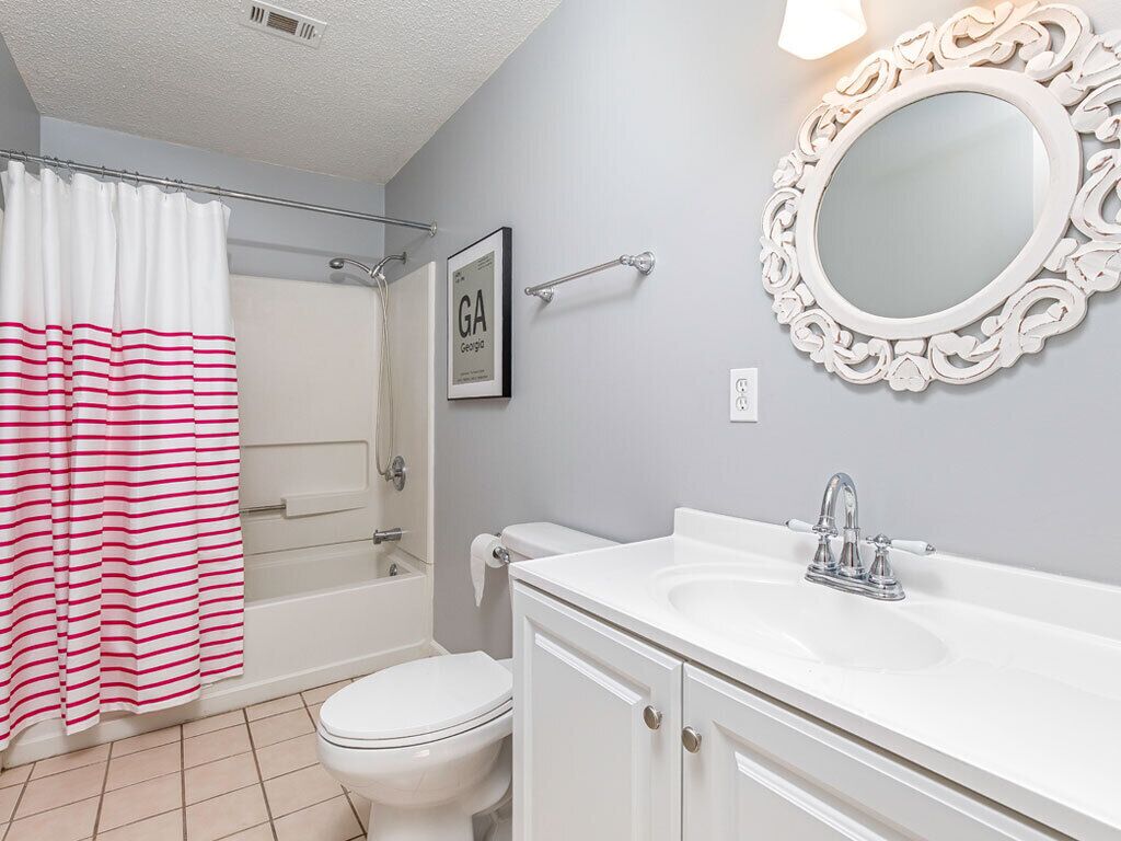 A bathroom with a white bathtub, a toilet, a sink with a mirror, and a shower curtain.