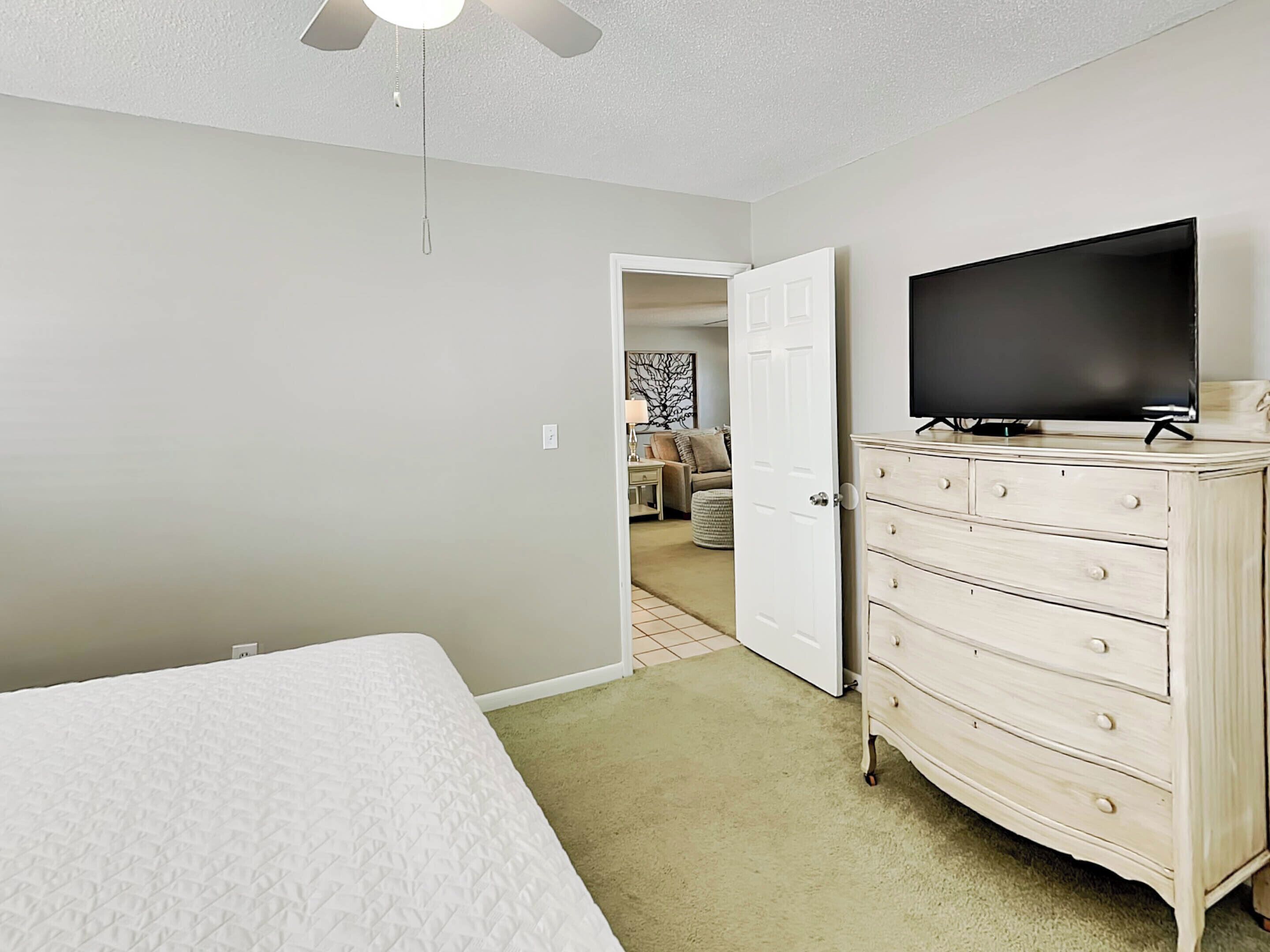 A bedroom with a bed, a dresser, a television, and a ceiling fan.