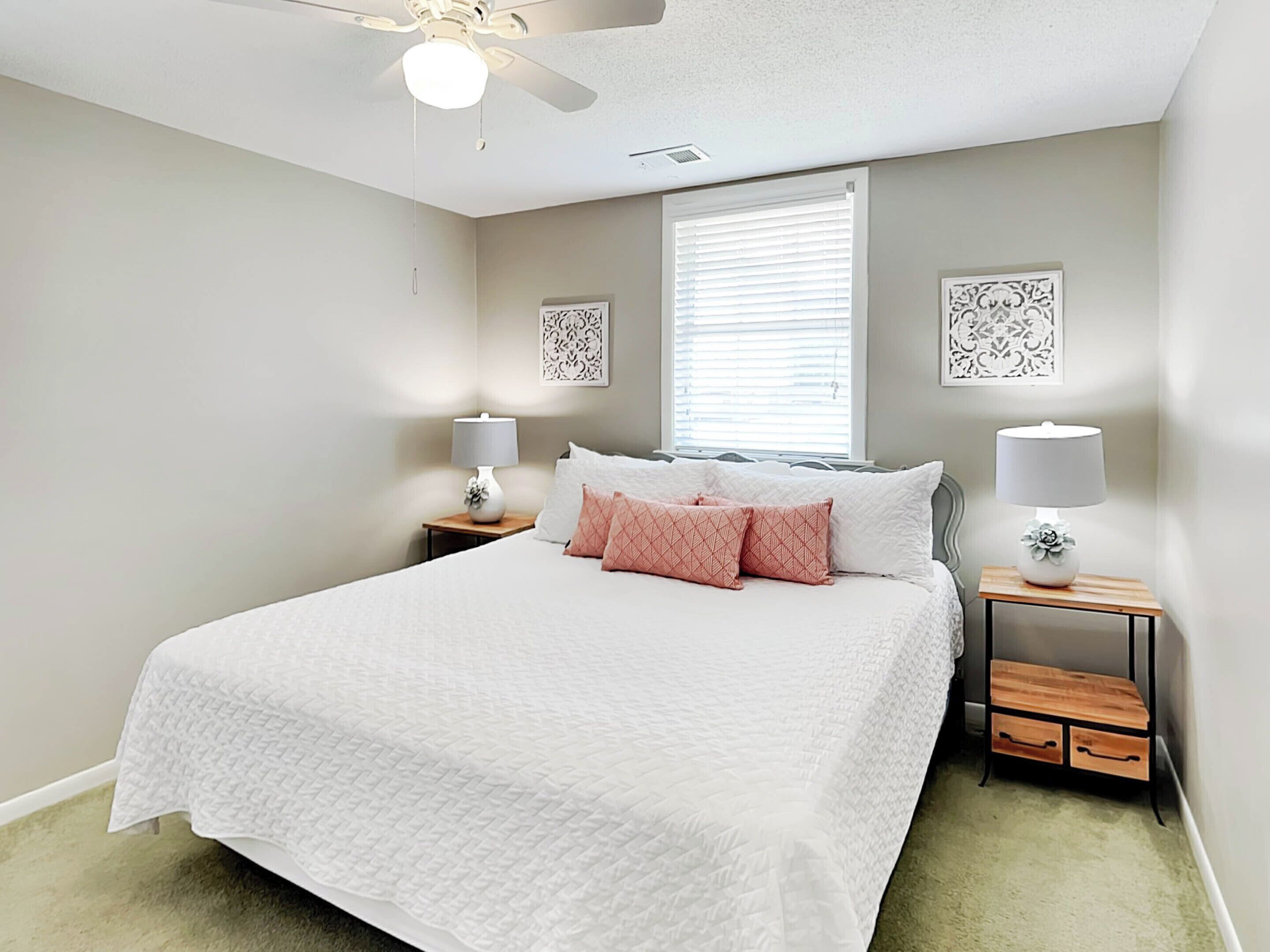 A bedroom with a bed, two bedside tables, a ceiling fan, and a window with blinds.