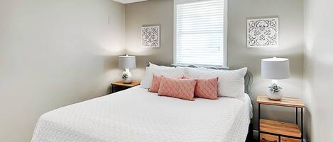 A bedroom with a bed, two bedside tables, a ceiling fan, and a window with blinds.