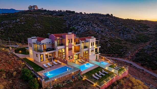 A modern multi-story villa with a swimming pool, multiple balconies, and a view of the surrounding hilly landscape. - Villa Mari Chania with ecologic private pool and amazing view. (Chania)