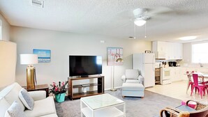 A modern living room with a sofa, coffee table, and a television. There is a dining area with a table and chairs, and a kitchen in the background. - Latitude Adjustment B Tybee Vacation Rentals (Tybee Island)