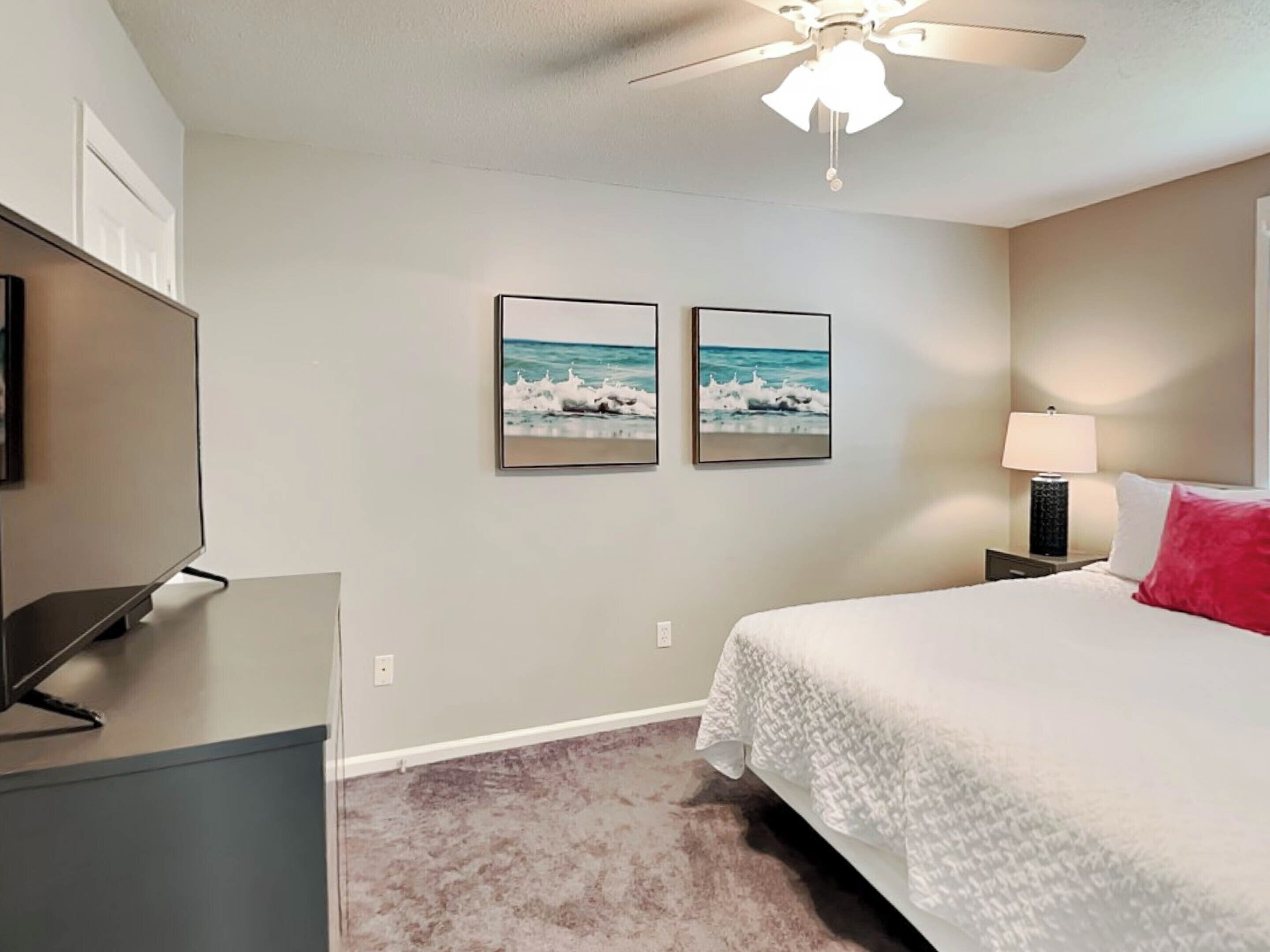 A bedroom with a bed, a ceiling fan, a TV, and two framed pictures on the wall.