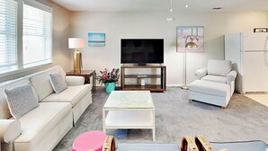 A living room with a sofa, a coffee table, a TV on a stand, a chair, and a lamp. - Latitude Adjustment B Tybee Vacation Rentals (Tybee Island)