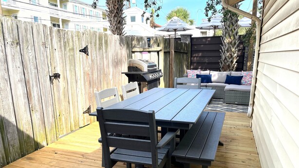 A wooden deck with a table and benches, a grill, and a covered seating area. - Latitude Adjustment B Tybee Vacation Rentals (Tybee Island)