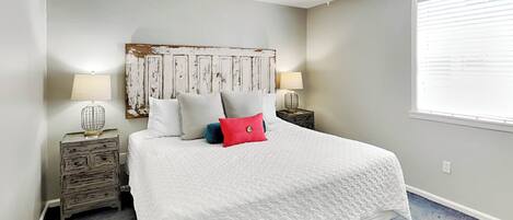 A bedroom with a large bed, two bedside tables with lamps, a ceiling fan, and a window with blinds.