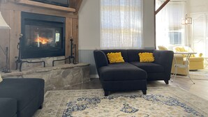 A living room with a fireplace, a sofa with yellow cushions, and a patterned rug. - The Inn at Dirickson Creek - Room Three (Frankford)