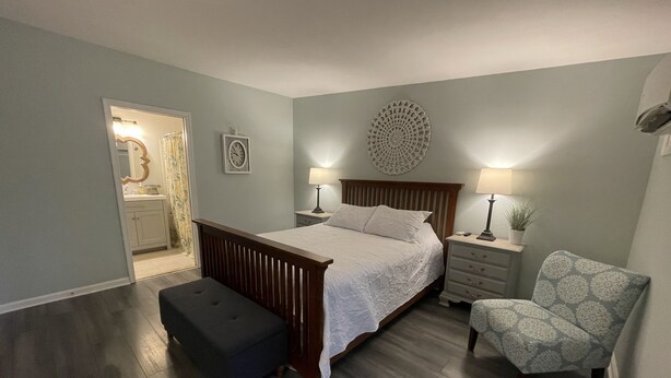 A bedroom with a wooden bed, a bench, a chair, a nightstand, and a wall clock. - The Inn at Dirickson Creek - Room Three (Frankford)