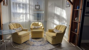 A cozy room with three yellow armchairs, a small round table, and a large window with sheer curtains. - The Inn at Dirickson Creek - Room Three (Frankford)