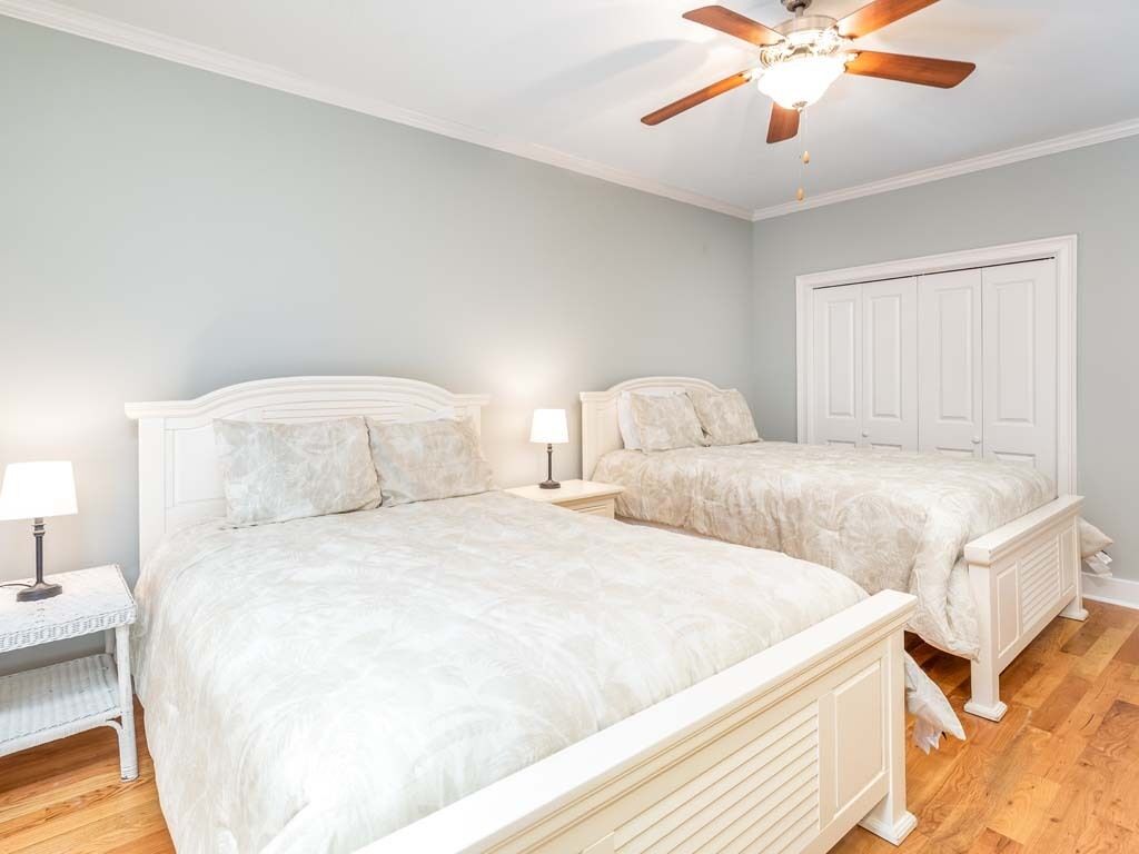 Une chambre avec deux lits, un ventilateur de plafond et une armoire blanche.