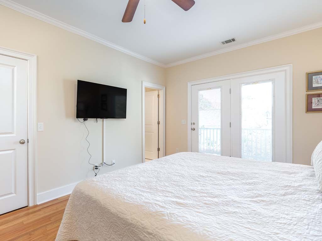 Ein Schlafzimmer mit einem großen Bett, einem Deckenventilator, einem Wand-Fernseher und einer Tür, die auf einen Balkon führt.