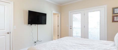 Ein Schlafzimmer mit einem großen Bett, einem Deckenventilator, einem Wand-Fernseher und einer Tür, die auf einen Balkon führt.