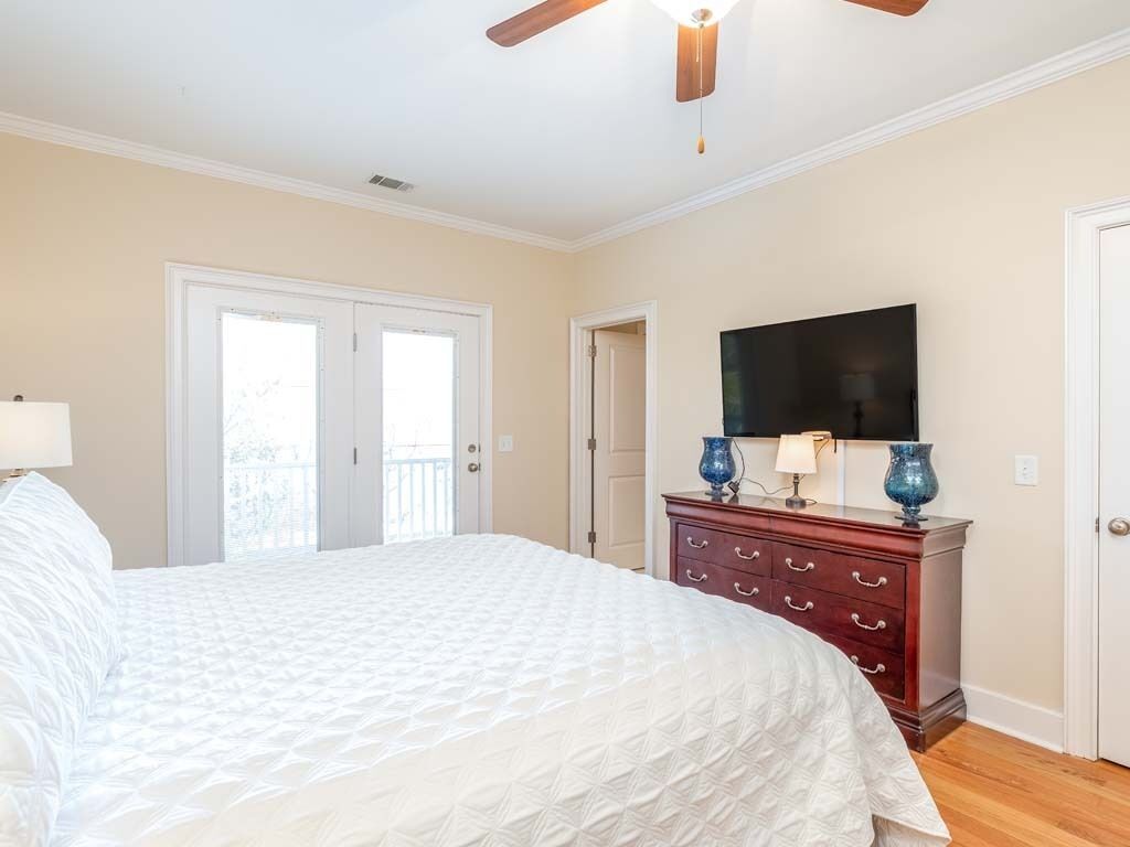 A bedroom with a large bed, a dresser, a television, and a ceiling fan.