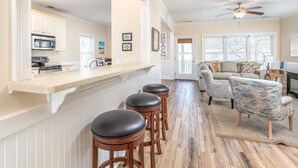 A spacious kitchen with a bar area, wooden stools, and a dining area with a patterned armchair. - Lazy Dayz Tybee Vacation Rentals (Tybee Island)