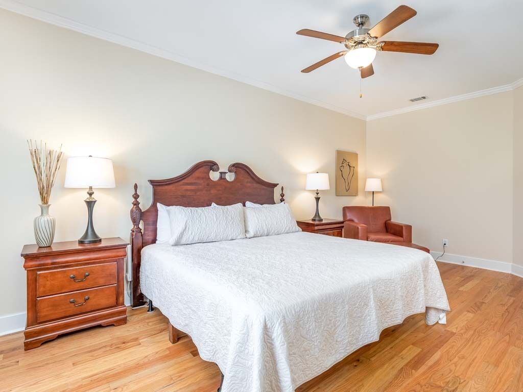 A bedroom with a wooden bed, two bedside tables with lamps, a ceiling fan, and a chair.
