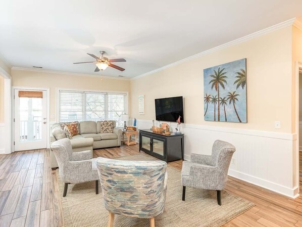 A living room with a sofa, two armchairs, a coffee table, a TV, and a ceiling fan. - Lazy Dayz Tybee Vacation Rentals (Tybee Island)