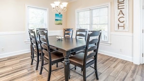 A dining room with a dark wooden table and chairs, a chandelier, and a "BEACH" sign on the wall. - Lazy Dayz Tybee Vacation Rentals (Tybee Island)