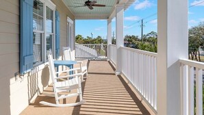 A covered porch with a ceiling fan, white railings, and a view of the surrounding landscape. - Lazy Dayz Tybee Vacation Rentals (Tybee Island)