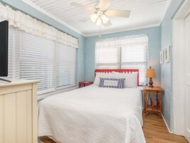 A bedroom with a bed, a ceiling fan, a nightstand, a lamp, and a TV.
